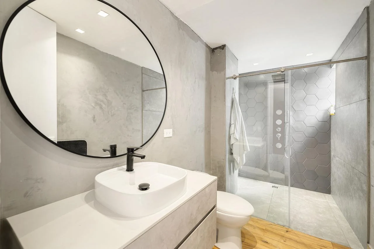 Baño de huéspedes contemporáneo en tonos grises con espejo circular y ducha de vidrio
