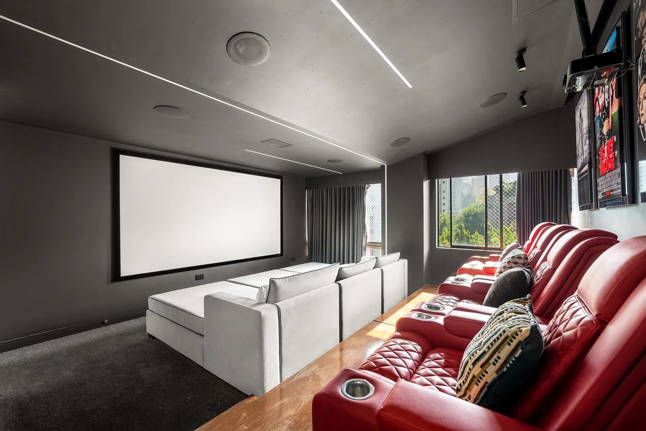 Cine privado con pantalla, sofás blancos y butacas reclinables rojas