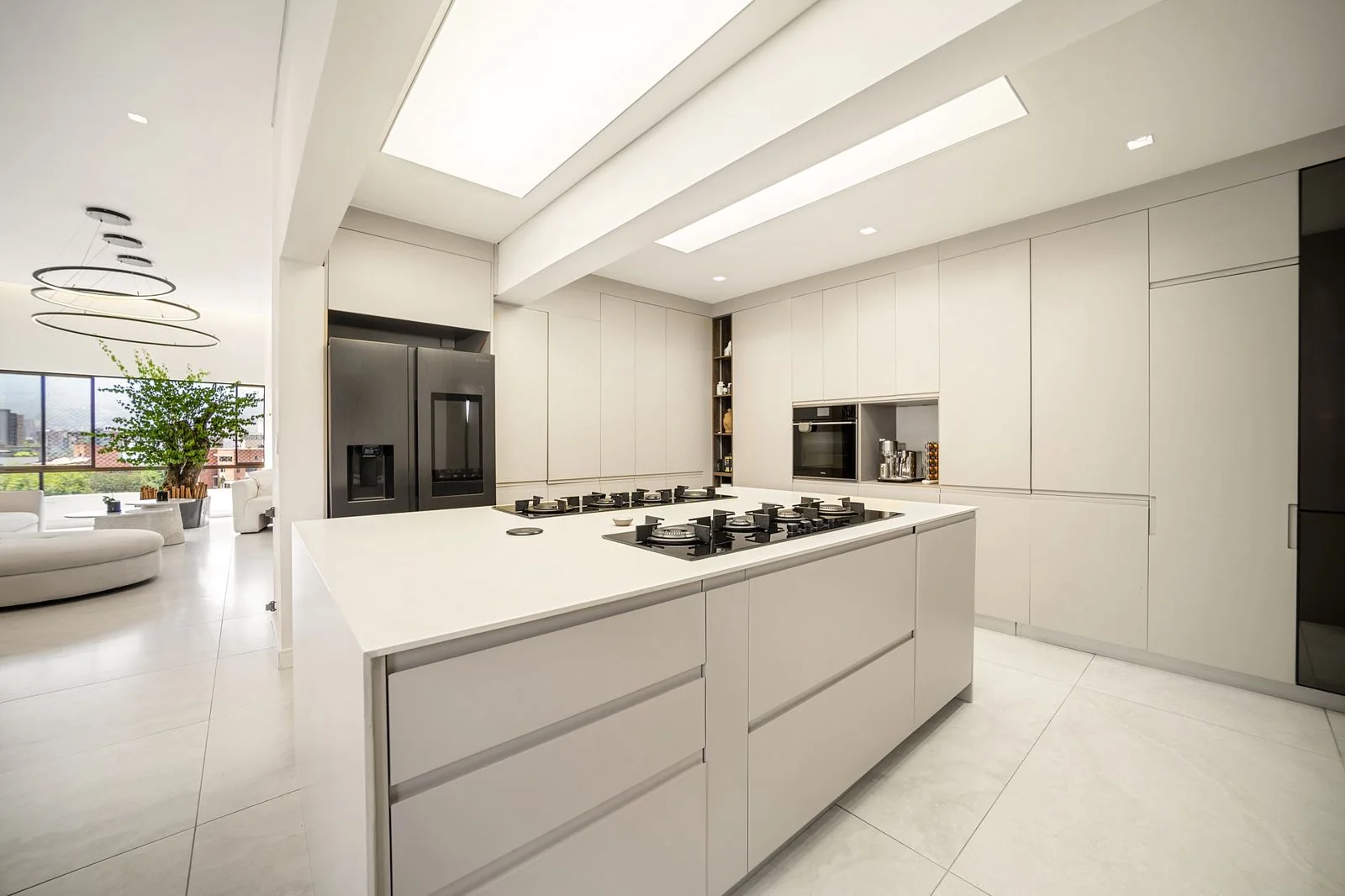 Cocina blanca con gran isla central, luz cenital y electrodomésticos integrados